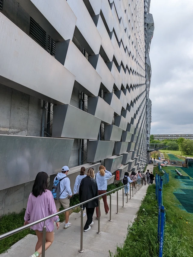 Students descend a long outdoor stairway beside CopenHill’s striking facade of stacked aluminum blocks.