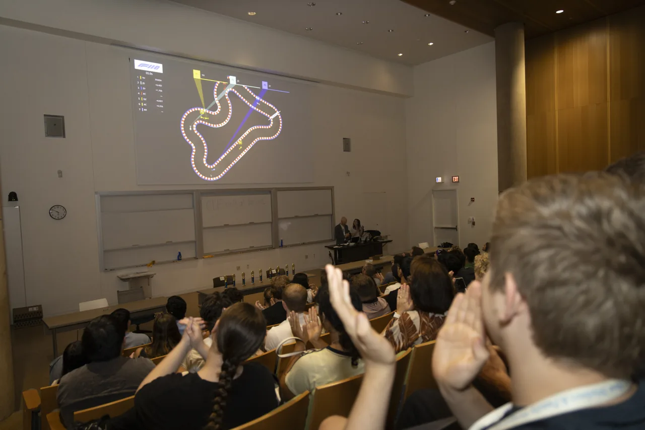 A projected race circuit in a lecture hall, with audience members applauding