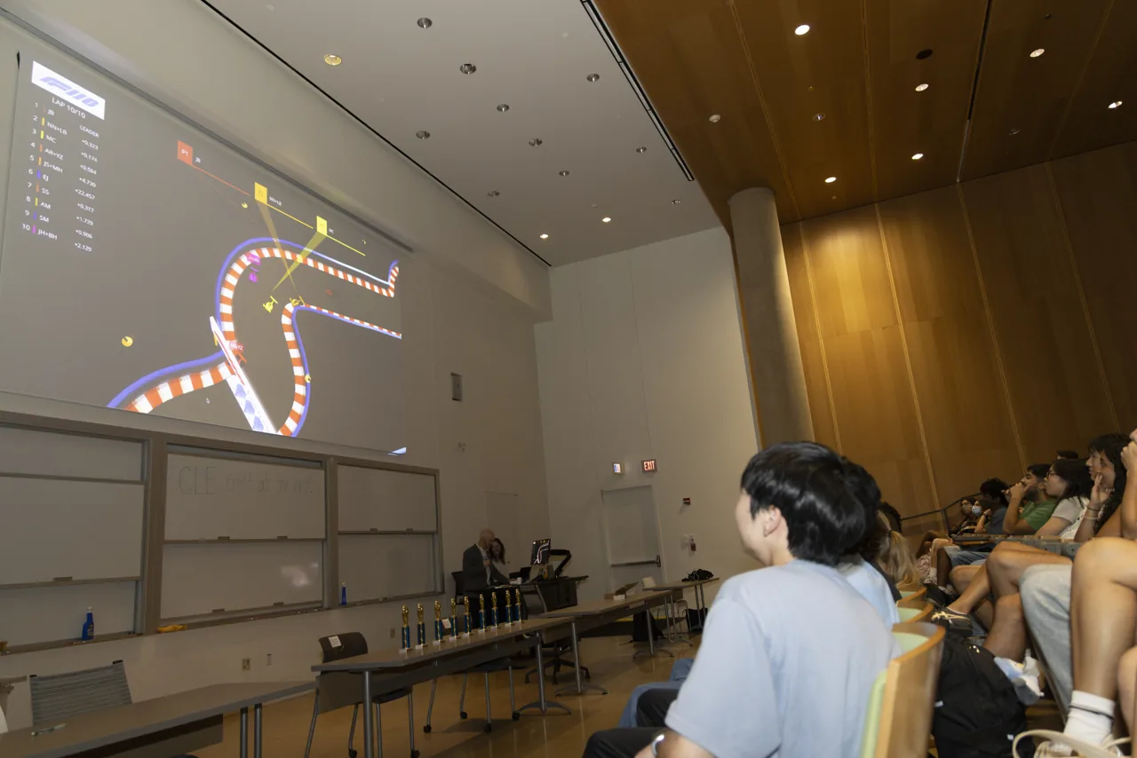A race circuit projected above a lecture hall as people watch from the audience